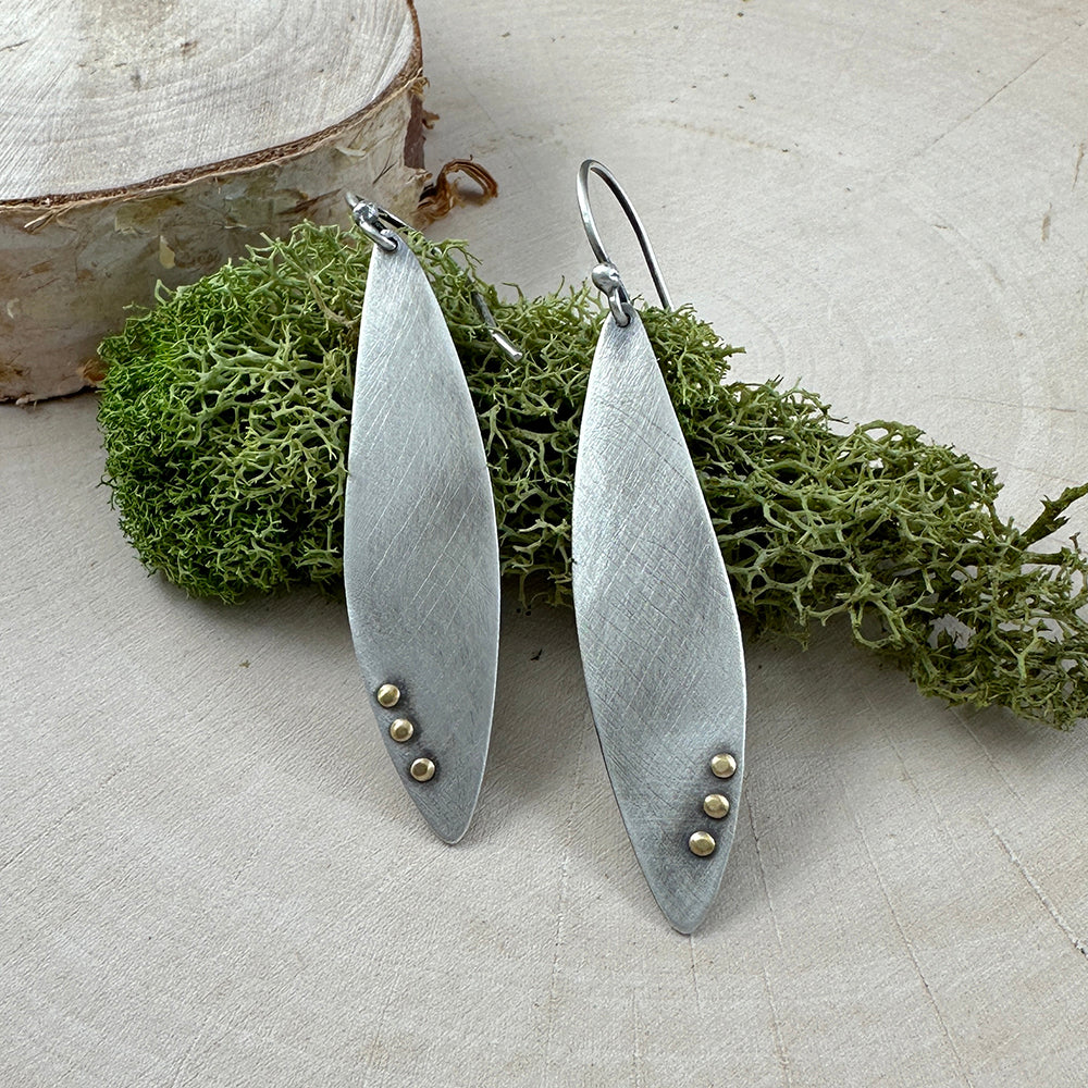 Sterling Silver wing shaped earrings with a brushed finish and brass rivet details all with a patina